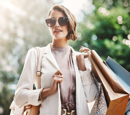 Stilvolle Frau mit Sonnenbrille und Einkaufstüten im Freien.