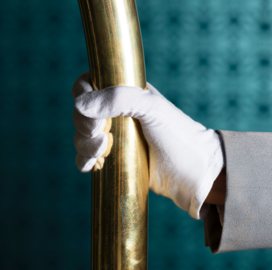 Die Hand eines Concierges in einem weißen Handschuh, die eine goldene Stange hält.